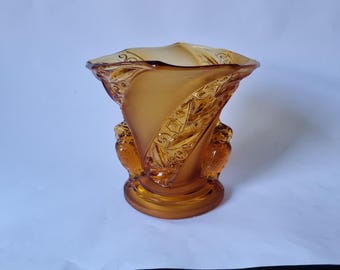 May include: An amber-coloured glass vase featuring a wide, flared rim and a swirling, textured body. The exterior surface displays intricate embossed patterns and two prominent, sculpted owl figures integrated into the base of the vessel.
