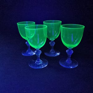 Op de afbeelding: Vier groen getinte wijnglazen met blauwe stelen en voetjes staan op een donkerblauwe ondergrond. De glazen hebben een afgeronde komvorm en een klassiek steelontwerp.