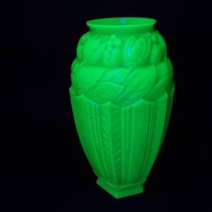May include: A bright, neon green art deco vase with a detailed floral and leaf design. The vase has a wide, rounded top and a rectangular base. The intricate patterns and bright colour make it a striking decorative piece.