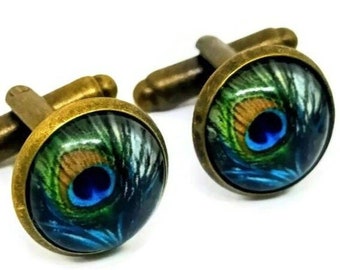 May include: A pair of cufflinks with a peacock feather design. The cufflinks are made of brass and have a round, glass-like surface with a peacock feather image.