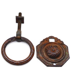 May include: An antique, rusty brown metal drawer pull set. The set includes a ring pull with a threaded bolt and a decorative, octagonal backplate with a floral design. The hardware has a weathered appearance.
