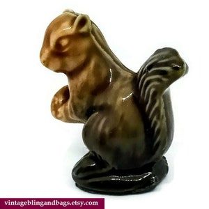 May include: A small ceramic figurine of a brown squirrel with a bushy tail. The squirrel is sitting on its haunches with its paws tucked in front of it.