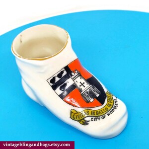May include: A white ceramic shoe-shaped trinket with a gold rim. The shoe features a colorful coat of arms with the text "CIVITAS IN BELLO IN PACE" and "CITY OF WORCESTER".