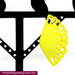May include: A pair of yellow earrings with a lacy design. The earrings are displayed on a black earring stand.