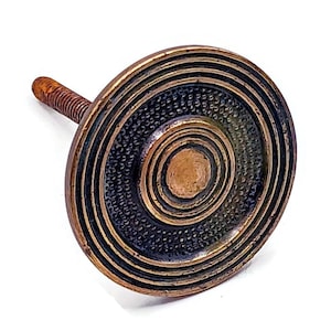 Könnte beinhalten: Ein bronzefarbener Schrankknauf mit kreisförmigem Design. Der Knauf hat konzentrische Ringe und eine strukturierte Mitte mit einem Gewindeschaft zur Befestigung. Die Hardware hat eine antike oder Vintage-Ästhetik.