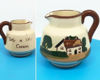 Könnte beinhalten: Ein kleiner, cremefarbener Keramik-Milchkännchen mit braunem Henkel. Es ist handbemalt mit einer Szene eines Hauses mit braunem Dach und einem grünen Baum. Der Text "Take a little Cream" ist auf der Vorderseite geschrieben.