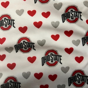 May include: A white fabric featuring a repeating pattern of the Ohio State University logo in red, black, and white, interspersed with numerous small solid red hearts and smaller solid grey hearts scattered across the entire surface.