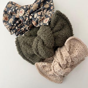 May include: Three fabric headbands in different styles. One headband is a floral print with a dark background, another is a dark green fuzzy fabric, and the last is a light beige headband with a lacy pattern.