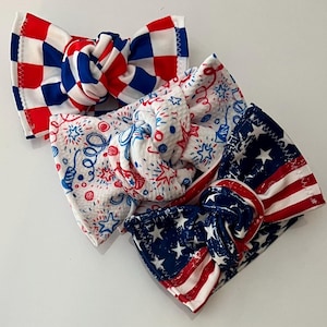 Op de afbeelding: Drie geknoopte hoofdbanden met patriottische ontwerpen. Eén heeft een rood-blauw dambordpatroon, één is wit met rode en blauwe vuurwerkillustraties en één toont een verweerde Amerikaanse vlagprint met witte sterren en rode strepen.