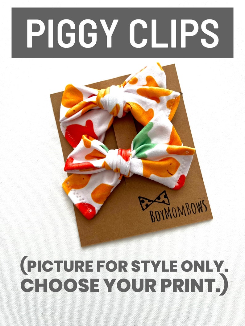 May include: Two fabric hair bows with a white background and a pattern of orange and yellow shapes. The bows are attached to a brown card with the text "PIGGY CLIPS" at the top and "BOYMOMBOWS" at the bottom. The text "(PICTURE FOR STYLE ONLY. CHOOSE YOUR PRINT.)" is also visible.