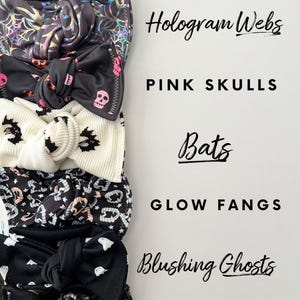 May include: A set of six black and white patterned headbands with different Halloween-themed designs. The designs include skulls, bats, ghosts, and webs. The headbands are arranged vertically with the text "Frida Skulls", "Hologram Webs", "Pink Skulls", "Bats", "Glow Fangs", "Blushing Ghosts", and "Skulls & Lilac" written next to each headband.