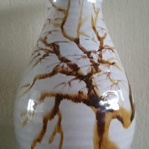 Op de afbeelding: Een witte keramische vaas met een bruin boomontwerp. De vaas heeft een rond lichaam en een smalle hals.