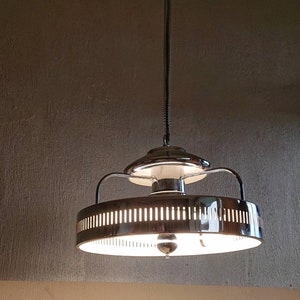 Op de afbeelding: Een chromen plafondlamp met een ronde, witte, matte glazen kap en een decoratieve metalen ring rond de kap.