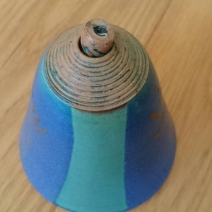 Op de afbeelding: Een blauwe en groene keramische bel met een bruine bovenkant. De bel heeft een getextureerd oppervlak en een afgeronde vorm.