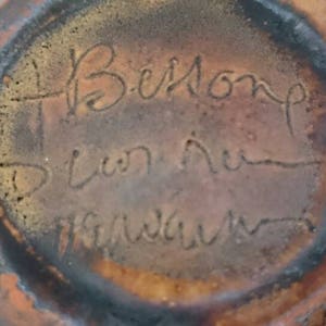 Pode incluir: Close-up da parte inferior de um pote de cerâmica marrom com a inscrição "Belmont, S. Van Ru, Hawaii" em tinta preta.