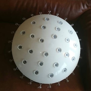 Op de afbeelding: Een witte plafondlamp met een ronde, koepelvormige kap. De kap is bedekt met kleine, heldere, kristal-achtige accenten.