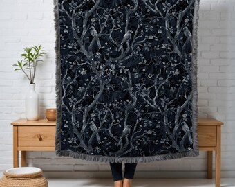 Può includere: Una coperta in bianco e nero con un motivo ripetitivo di uccelli e rami. La coperta ha un bordo in pelliccia sintetica grigia.