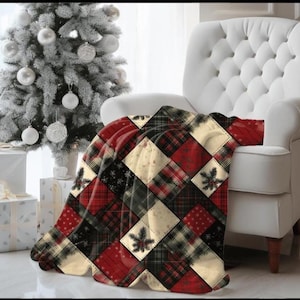 May include: A red, black, and cream patchwork throw blanket draped over a white armchair. The blanket features a variety of patterns, including plaid, polka dots, and floral designs. A frosted Christmas tree and wrapped gifts are in the background.