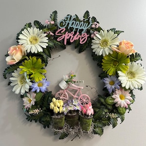 Może przedstawiać: Wiosenny wianek z różnorodnymi kolorowymi kwiatami, w tym białymi stokrotkami, różowymi różami oraz niebieskimi i żółtymi kwiatami. Różowy rower i napis "Happy Spring" również się na nim znajdują.