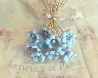 May include: A bunch of light blue flower-shaped embellishments with silver wire stems. The flowers have a small clear rhinestone in the centre.