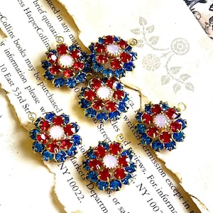 May include: Five floral-shaped jewelry components. Each component features a central white stone surrounded by red and blue gemstones, set in a gold-tone metal. The components are arranged on a vintage paper background.