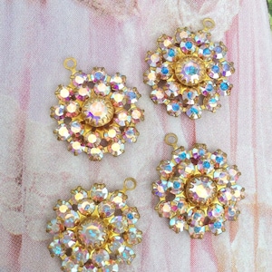 May include: Four gold-toned metal flower-shaped pendants with iridescent rhinestones. Each pendant has a loop at the top for hanging.