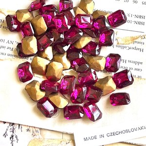 May include: A collection of faceted, rectangular, and golden-colored beads and deep magenta-colored rectangular gems. The gems are scattered on a background of aged paper with text. The gems are labeled "MADE IN CZECHOSLOVAKIA".