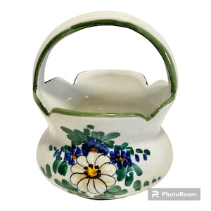 May include: A white ceramic basket with a green handle and floral design. The flowers are painted in shades of blue, green, white, and yellow.