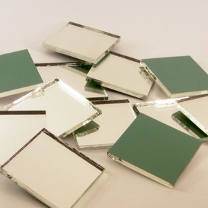 May include: A collection of square glass tiles with mirrored surfaces and green backing. The tiles are scattered, showcasing their reflective quality and the contrast between the mirrored front and the green back.