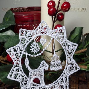Puede incluir: Adorno navideño blanco en forma de estrella con un diseño de encaje detallado. Dentro de la estrella hay un caballo, un copo de nieve, un corazón y un árbol de Navidad. El adorno está rodeado de vegetación, bayas rojas y una vela. El texto "MADAM HANDYCRAFT" es visible.