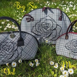 May include: Three handbags with a black and white plaid pattern and a rose design embroidered on the front. The bags are labeled "Party Girl", "Big Sis", and "Mini Miss". The bags have black and brown handles and are set on a bed of grass.