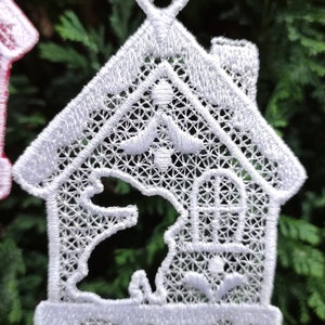 以下が含まれることがあります： ハート型のトップが付いた家の形をした白いレースのクリスマスオーナメント。家は窓と中にバードハウスがあります。