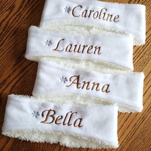 Puede incluir: Cuatro diademas de vellón blanco con un copo de nieve y un nombre bordado en cada una. Los nombres son Caroline, Lauren, Anna y Bella.