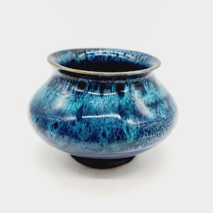 May include: A small, blue and green ceramic pot with a wide base and a rounded shape. The pot has a speckled glaze with a dark blue base and lighter green accents.