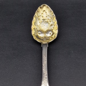 以下が含まれることがあります： パイナップルのエンボス加工が施された金メッキのボウルが付いた銀のスプーン。スプーンは、花柄の装飾的なハンドルが付いています。