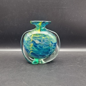 Puede incluir: Un jarrón de cristal transparente con cuerpo redondeado y cuello acampanado. El interior presenta un patrón arremolinado de colores azul, verde y amarillo. El jarrón tiene un exterior transparente y curvado, creando un efecto de doble pared único.