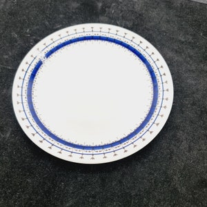 May include: A white ceramic plate with a blue and brown decorative border. The border features a repeating pattern of small blue flowers and brown lines.