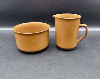 May include: A brown ceramic creamer and sugar bowl set. The creamer has a handle and the sugar bowl is round.