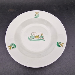 Puede incluir: Plato de cerámica blanca con forma de cuenco poco profundo. El plato presenta un diseño de tren pintado a mano en verde, amarillo y marrón, con elementos decorativos verdes y amarillos adicionales alrededor del borde. Un diseño encantador y caprichoso para niños.
