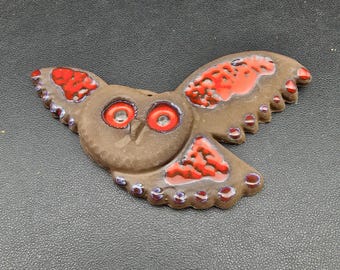 Könnte beinhalten: Braune Keramik-Eulenfigur mit ausgebreiteten Flügeln. Die Eule hat rote und orangefarbene Akzente auf den Flügeln und Augen. Die Flügel haben einen gewellten Rand mit kleinen lila Punkten. Ein dekorativer Artikel.