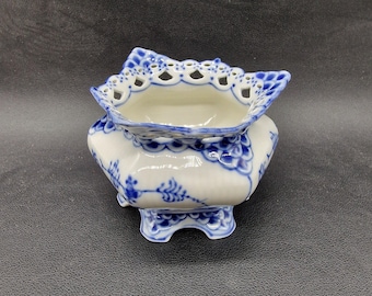 May include: A white porcelain sugar bowl with a blue and white floral design. The bowl has a scalloped edge and a lace-like design around the top. The bowl is on a black background.