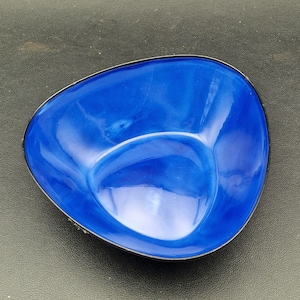 May include: A small, triangular-shaped blue dish with a glossy finish. The dish has a black rim and a smooth, curved interior. The dish is empty and appears to be made of ceramic or a similar material. The dish is designed for serving small portions of food.