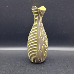 May include: A brown ceramic vase with a yellow interior and decorative yellow lines. The vase has a unique shape, with a narrow neck and a wider body. The design features horizontal and curved lines, creating a textured appearance.
