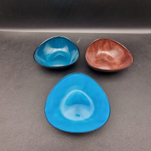 May include: Three triangular shaped bowls, one brown, two blue. The bowls are made of a glossy material and have a black rim.