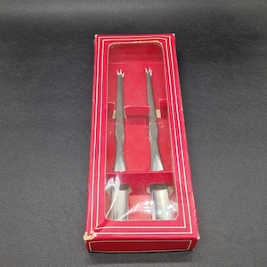 May include: Two silver-colored, pointed tools in a red box with a clear plastic window. The tools are in a vertical position and are parallel to each other.