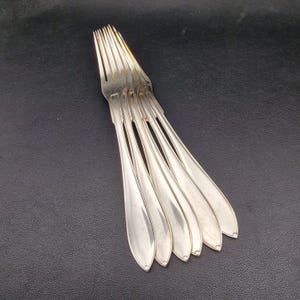 Może przedstawiać: Zestaw ośmiu srebrnych widelców ułożonych jeden na drugim. Widelce są wypolerowane i mają klasyczny design.