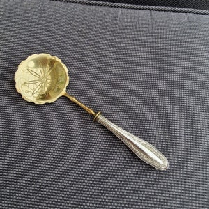 Puede incluir: Una cuchara de plata y oro con un mango decorativo y un cuenco redondo con un diseño floral.