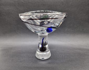 May include: A clear glass bowl with a black and blue design. The bowl has a wide, shallow base and a tall, slender stem.