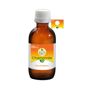 Op de afbeelding: Een bruine glazen fles met een witte dop die kamilleolie bevat. Het etiket is oranje en geel met de tekst "SSCP Botanicals" en "Chamomile Oil Pure & Natural".