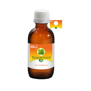 Può includere: Una bottiglia di vetro marrone con un tappo bianco, contenente olio di menta verde. L'etichetta è arancione e bianca con il testo "SSCP Botanicals" e "Spearmint Oil Pure & Natural".